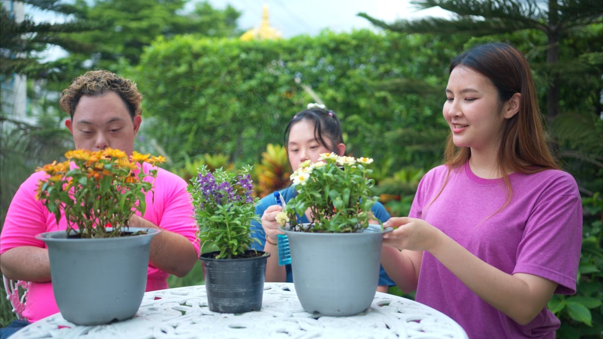 Three siblings helping to water and plant flowers together on a sunny day