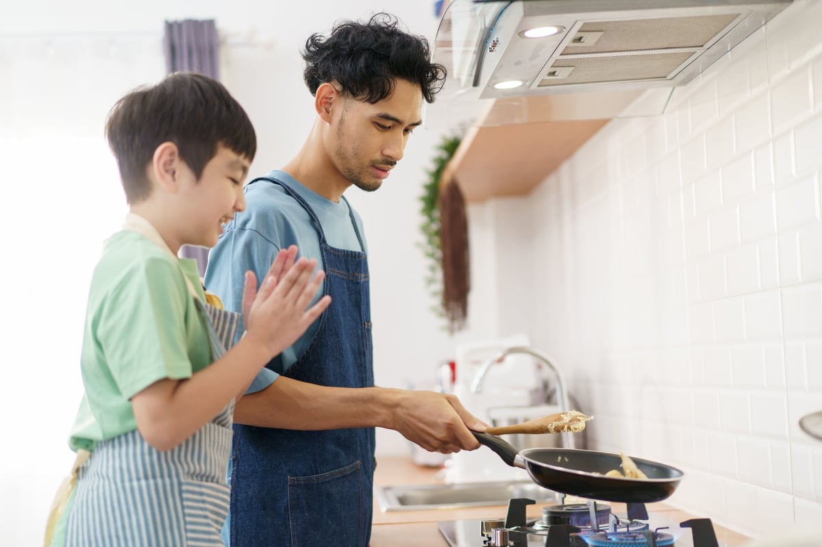 An Asian father and his young son sharing a joyful cooking moment at home on the weekend